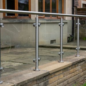 Toughened balustrade glass panels cut to size, clamped to stainless posts with a tubular handrail on a garden wall